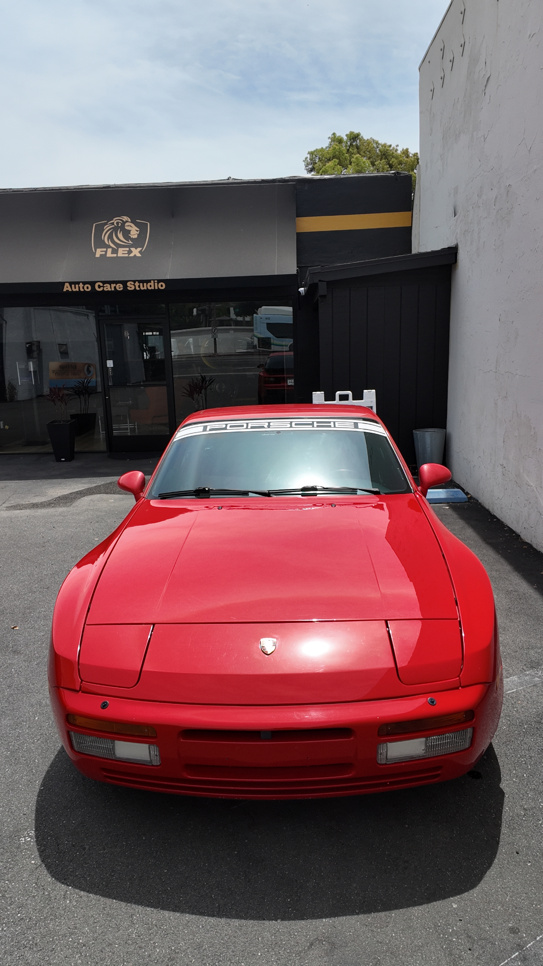 Red Porsche 944 Turbo head-on in front of the Flex Auto Care Studio entrance after professional window tinting